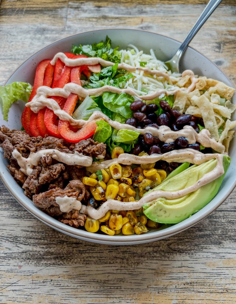 Southwest steak salad in a bowl with a chipotle lime dressing drizzled over the top