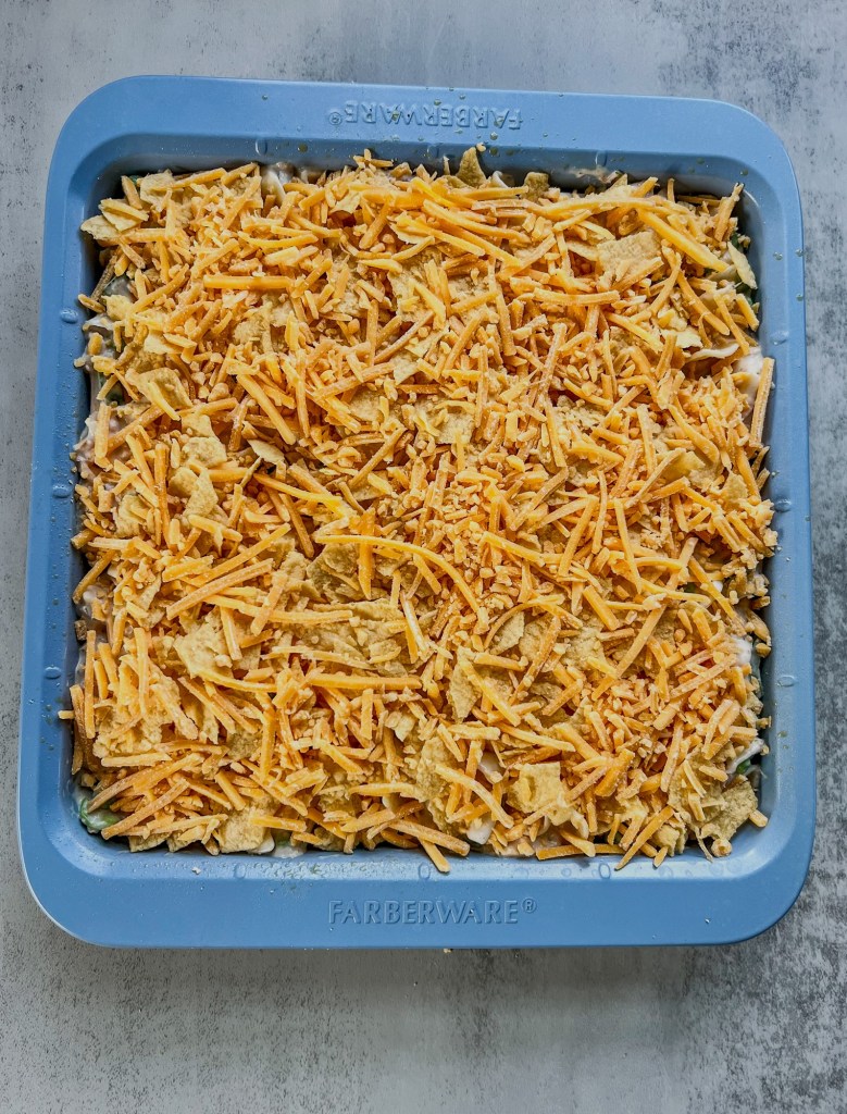 Spicy Tuna Noodle Casserole in a baking pan with shredded cheese on top before going into the oven