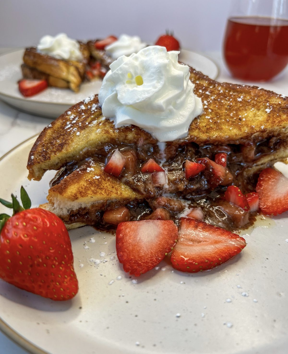 Strawberry and Nutella Stuffed French Toast on a plate with some whipped cream, powdered sugar, and strawberries
