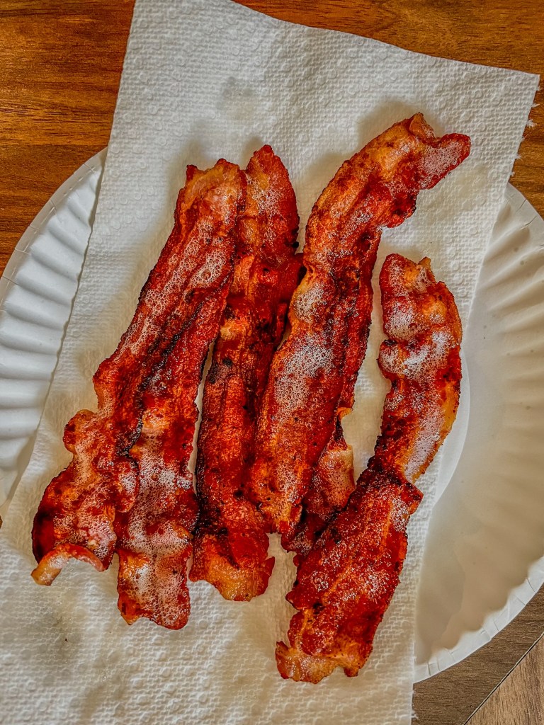 Cooked bacon on a paper plate with paper toweling underneath