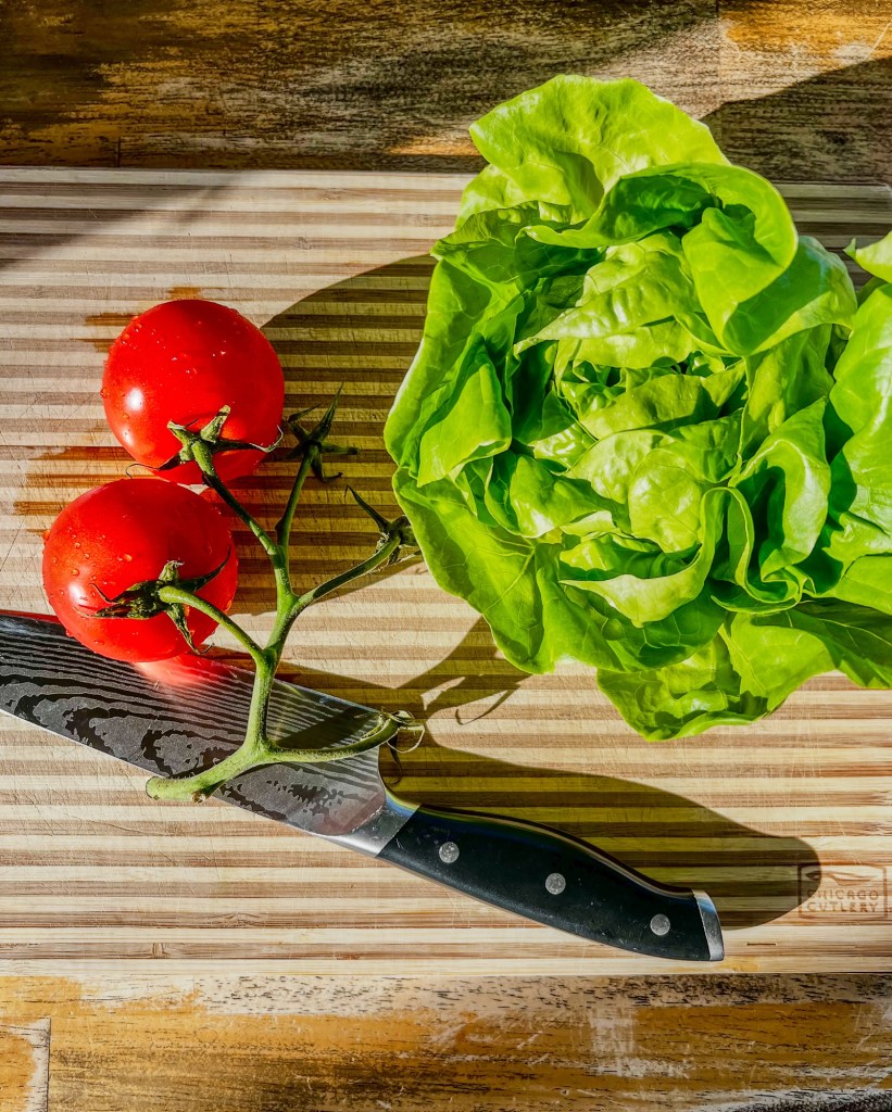 Tomatoes on the vine, artisan lettuce, and a chef knife on a wooden cutting board