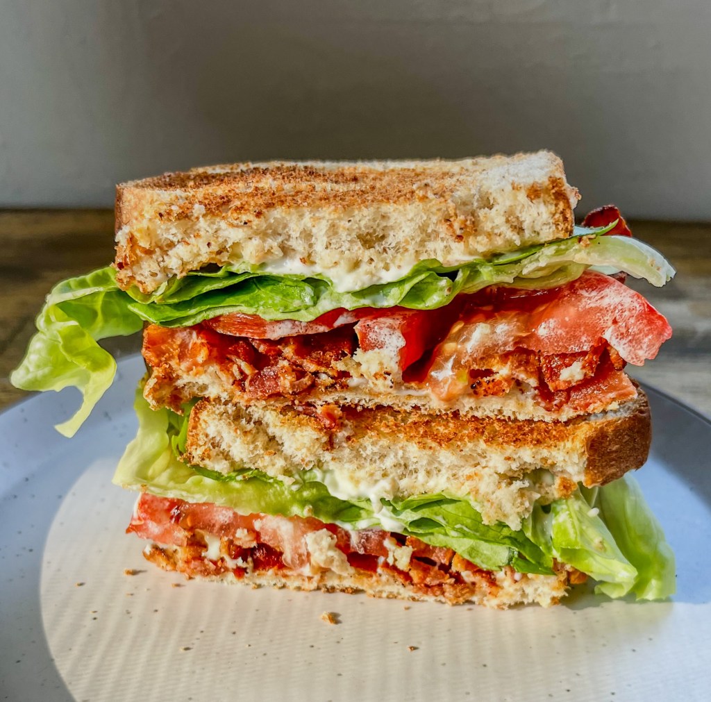 The ultimate blt that's been cut in half and stacked on a white plate