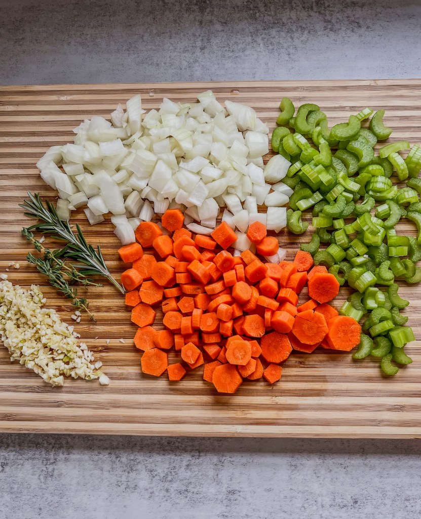 A bunch of veggies and herbs cut up on a cutting board to make a casserole