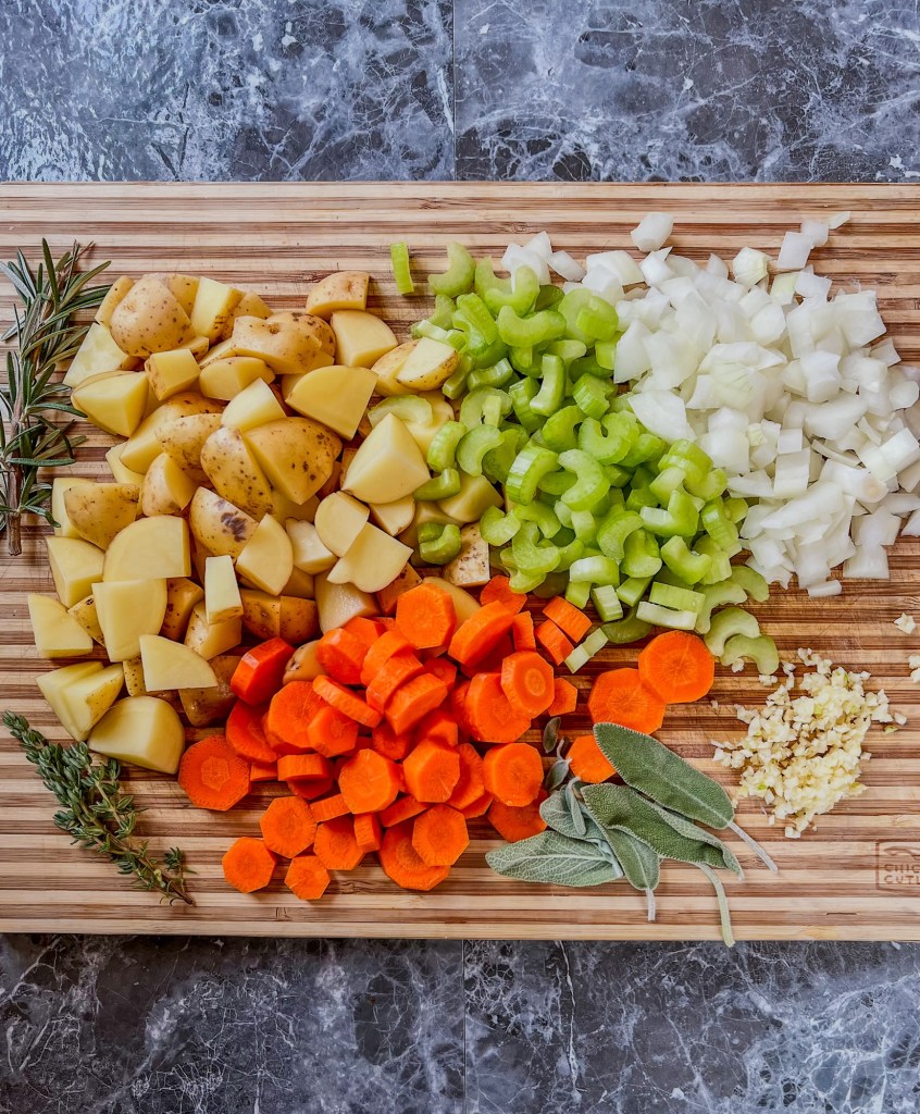 Fresh veggies cut up on a wooden cutting board with some fresh herbs off to the side