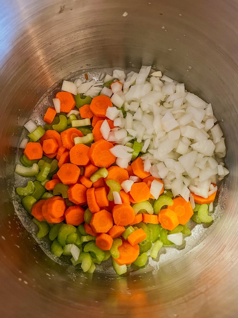 Vegetables, butter, and seasonings cooking in a large stockpot on the stove