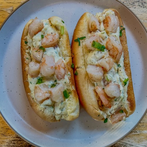 Warm shrimp roll with green onion, lemon juice, and parsley on top on a plate