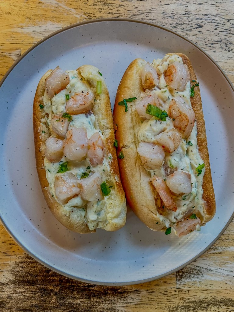 Warm shrimp roll with green onion, lemon juice, and parsley on top on a plate