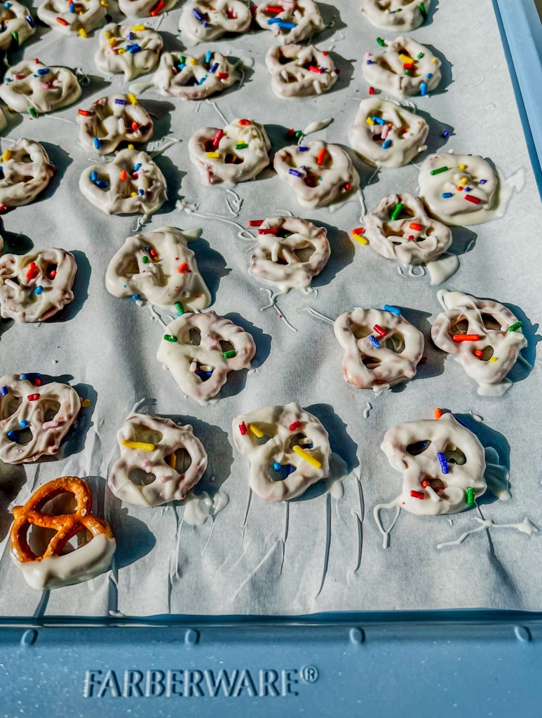 White chocolate covered pretzels with sprinkles on a blue baking sheet, hardening after coating