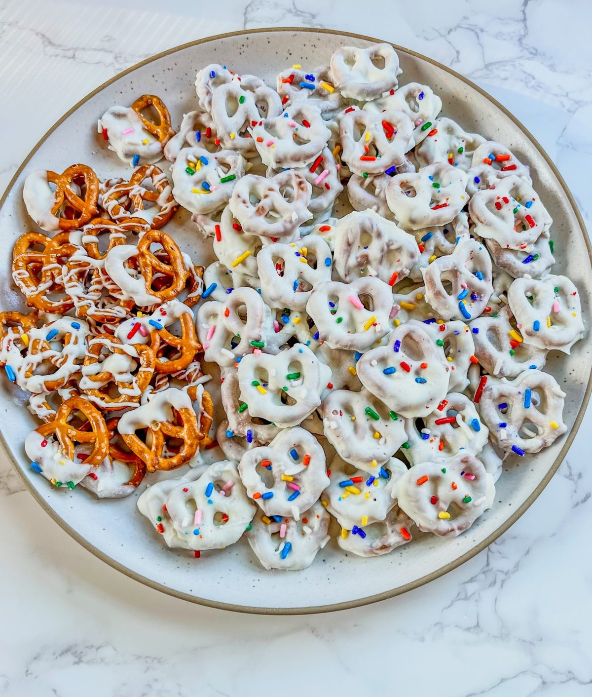 White chocolate covered pretzels on a white plate on a marble counter
