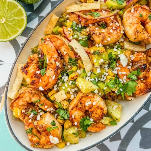Avocado Shrimp Salad in a dish with a wooden spoon scooping some out and some lime and avocado off to the side