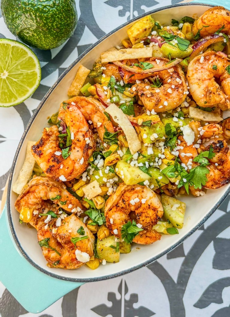 Avocado Shrimp Salad in a dish with a wooden spoon scooping some out and some lime and avocado off to the side