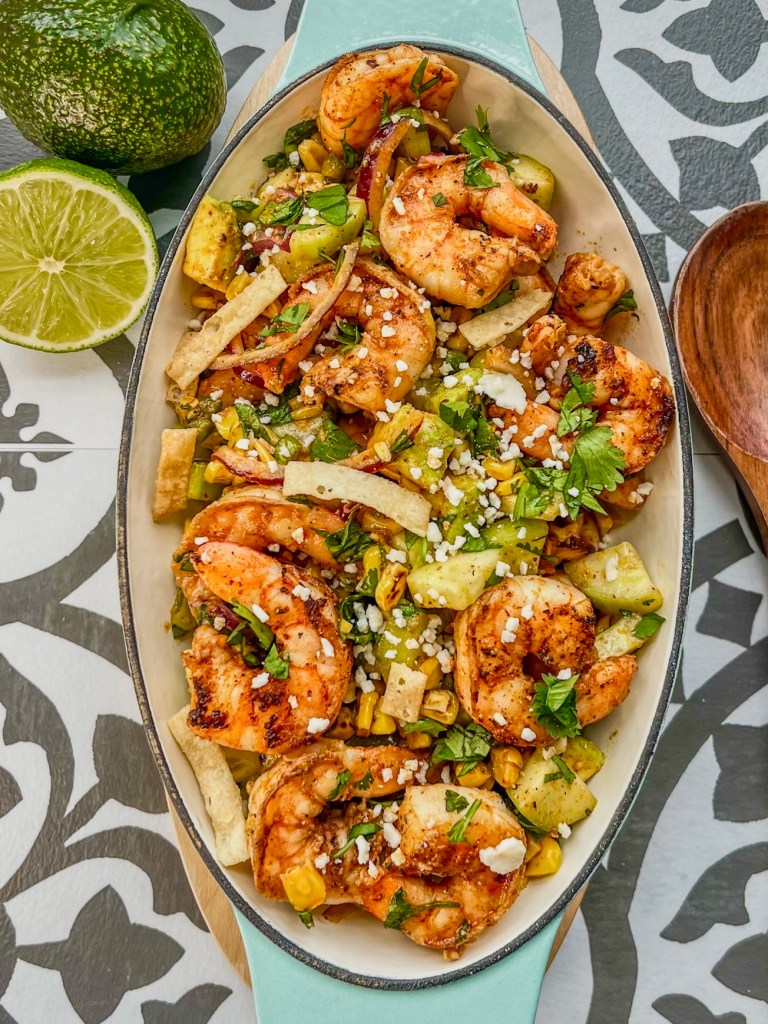 Shrimp salad in a serving dish with garnishes on top and some more lemon and avocado off to the side