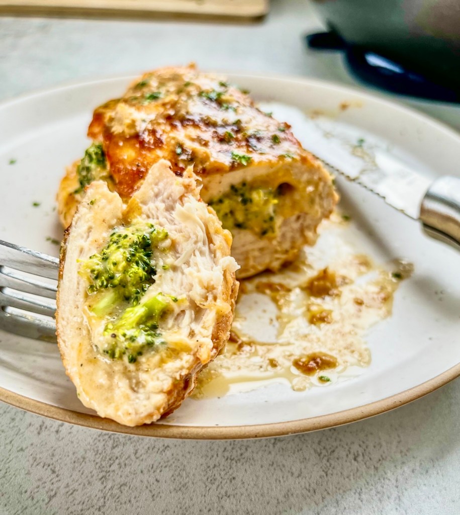 A broccoli cheddar stuffed chicken breast sliced on a plate with garlic Dijon sauce drizzled over the top
