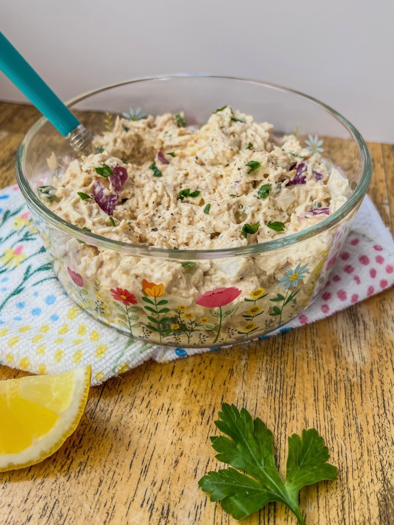Fresh chicken salad in a serving dish with some lemon and parsley off to the side