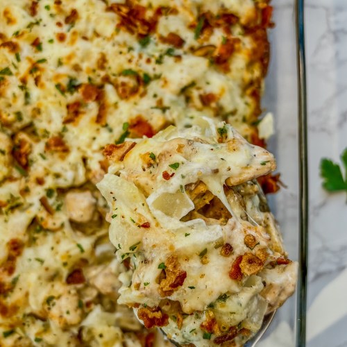 Chicken bacon potato bake in a baking dish with a serving spoon scooping some out.