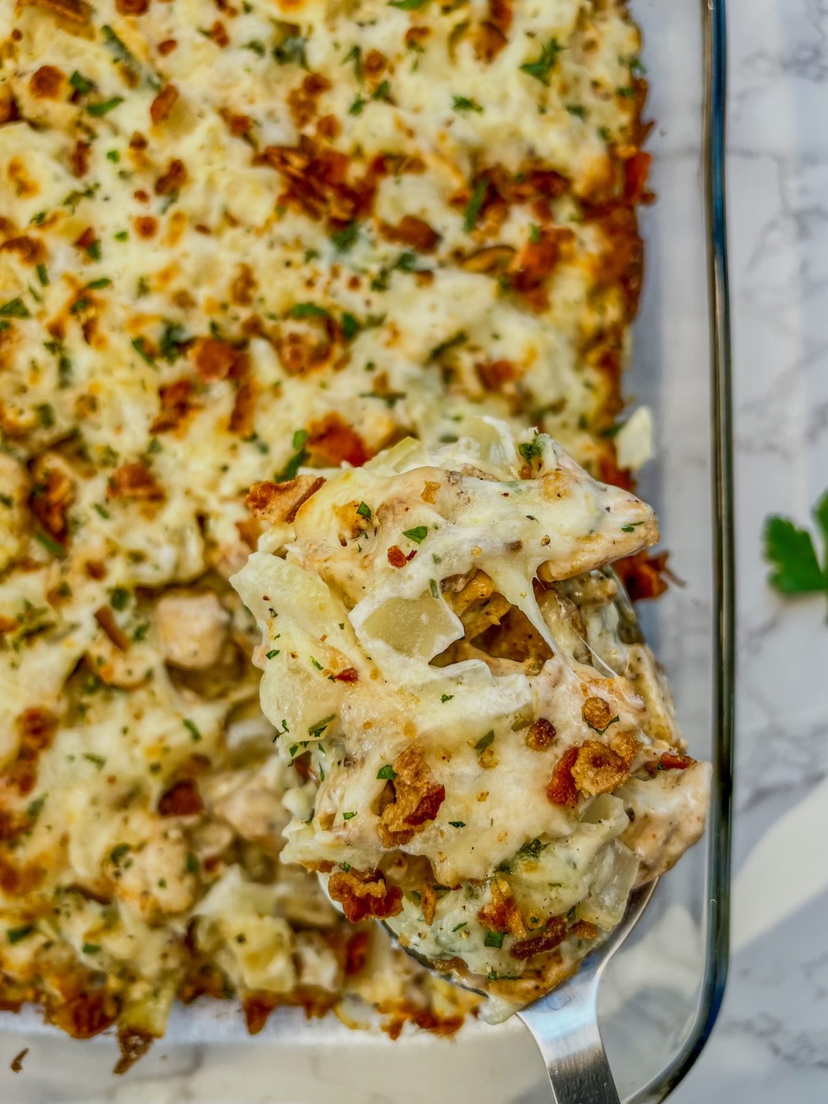 Chicken bacon potato bake in a baking dish with a serving spoon scooping some out.