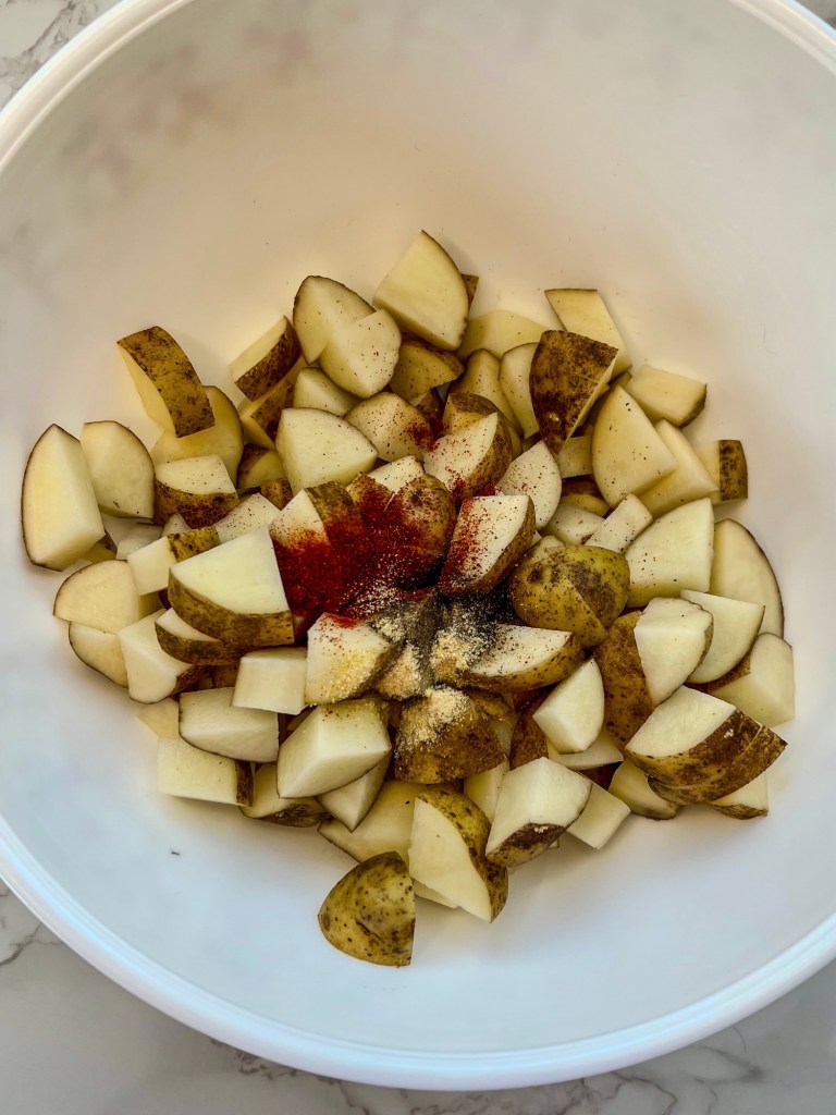 Diced potatoes in a mixing bowl with salt, pepper, paprika, garlic powder, and olive oil