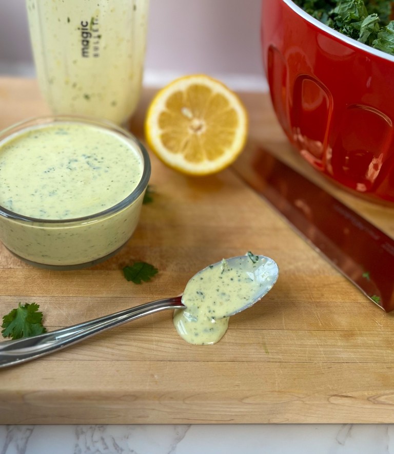 Cilantro lemon dressing in a glass dish on a wooden cutting board with a spoonful of it nearby