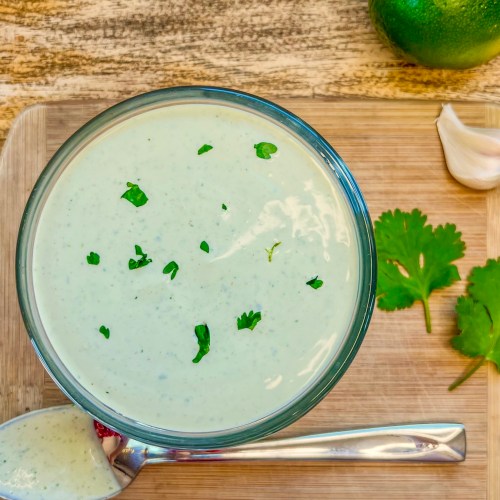 Cilantro lime crema in a dish with some cilantro for garnish and some garlic and lime off to the side