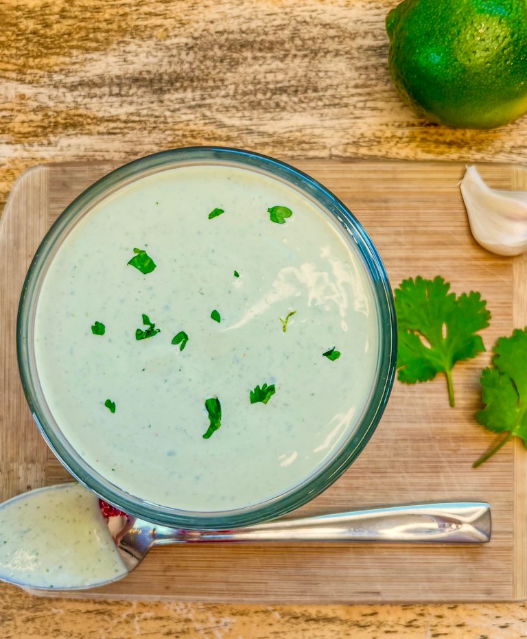 Cilantro lime crema in a dish with some cilantro for garnish and some garlic and lime off to the side