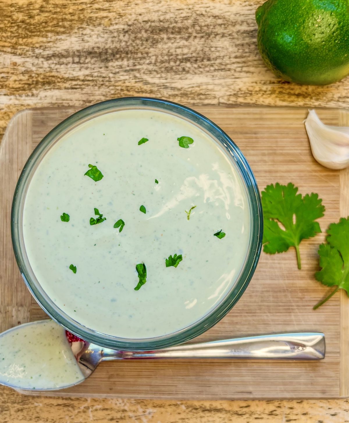 Cilantro lime crema in a dish with some cilantro for garnish and some garlic and lime off to the side