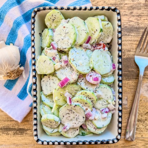 Creamy cucumber salad in a bowl with some garlic and a spoon off to the side