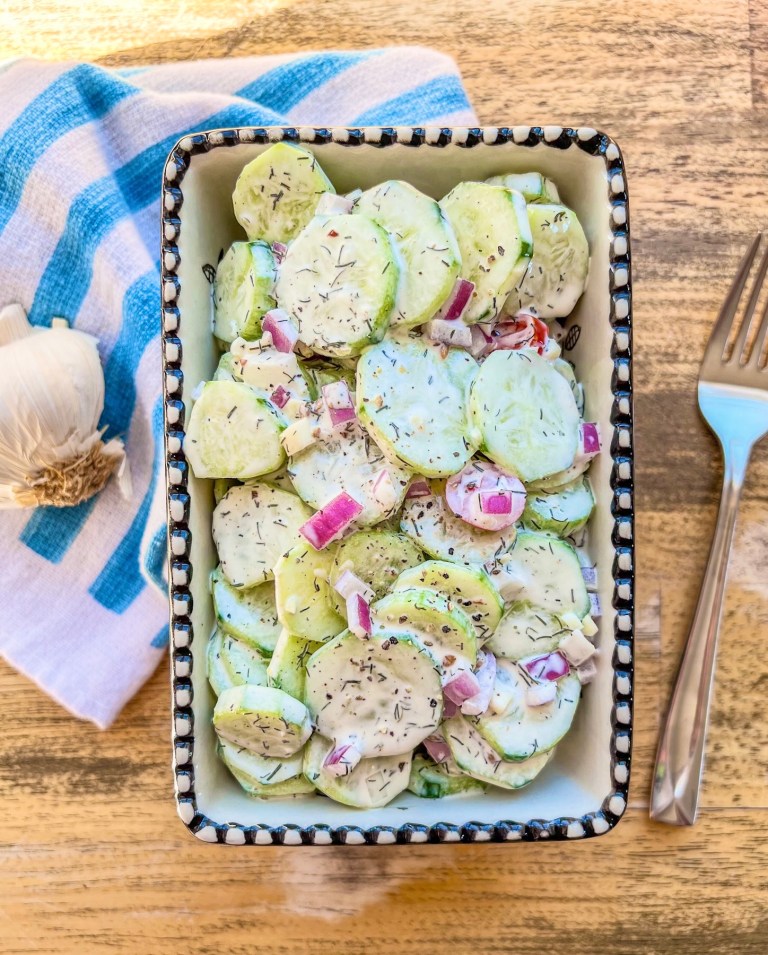 Creamy cucumber salad in a bowl with some garlic and a spoon off to the side