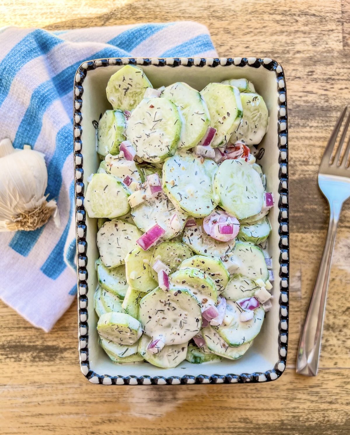 Creamy cucumber salad in a bowl with some garlic and a spoon off to the side