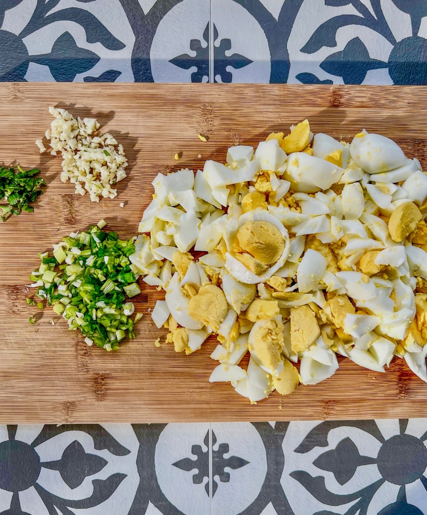Eggs, green onion, garlic, and parsley cut up on a wooden cutting board