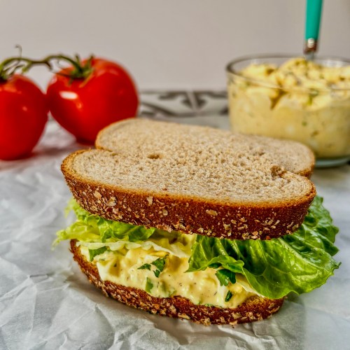 Creamy egg salad smeared on bread with some fresh lettuce to make a sandwich
