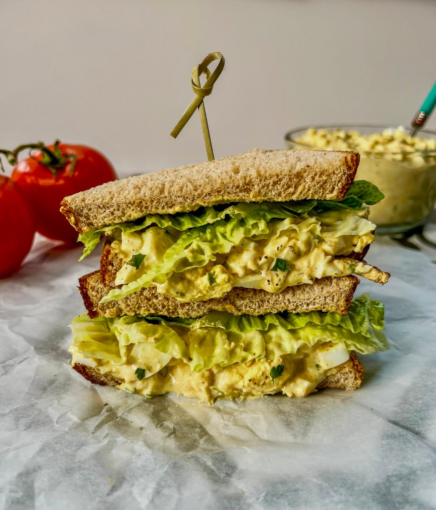 A sandwich sliced in half for lunch with some tomatoes and more sandwich filling off to the side
