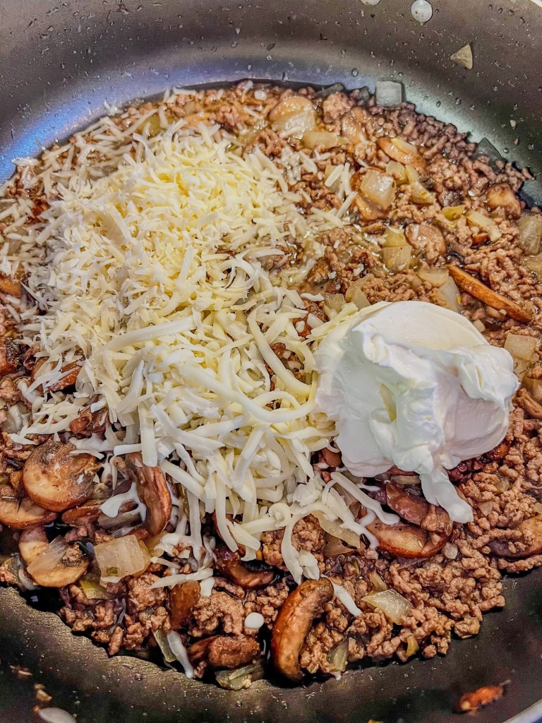 Ground beef mixture with sour cream, mozzarella, and parmesan cheese being stirred in