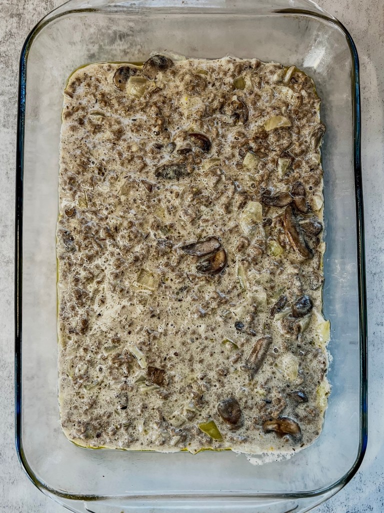 Tater tot casserole being assembled in a pan
