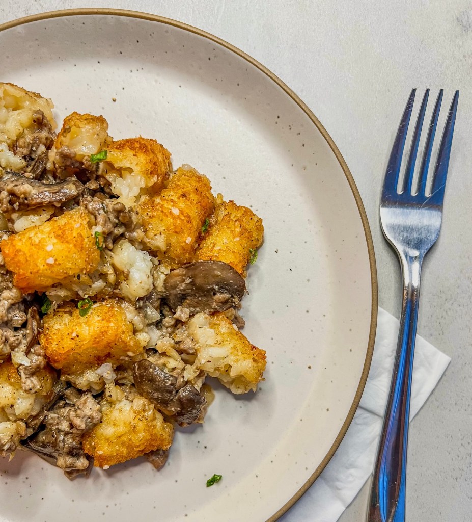 Tater tot hotdish with thinly sliced chives on a plate with a fork next to it