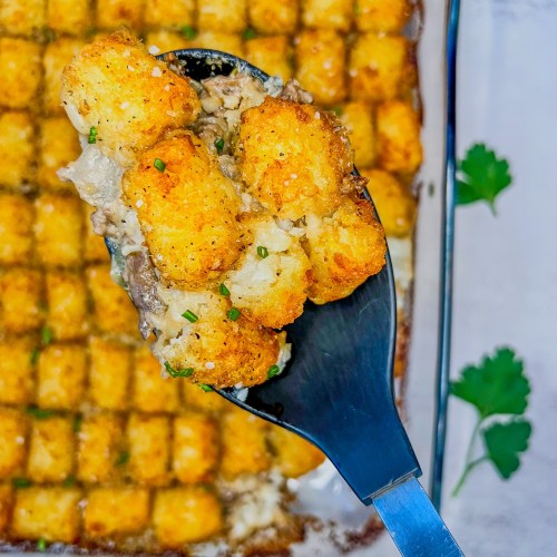 Creamy mushroom tater tot casserole in a baking dish with a spoon scooping some out