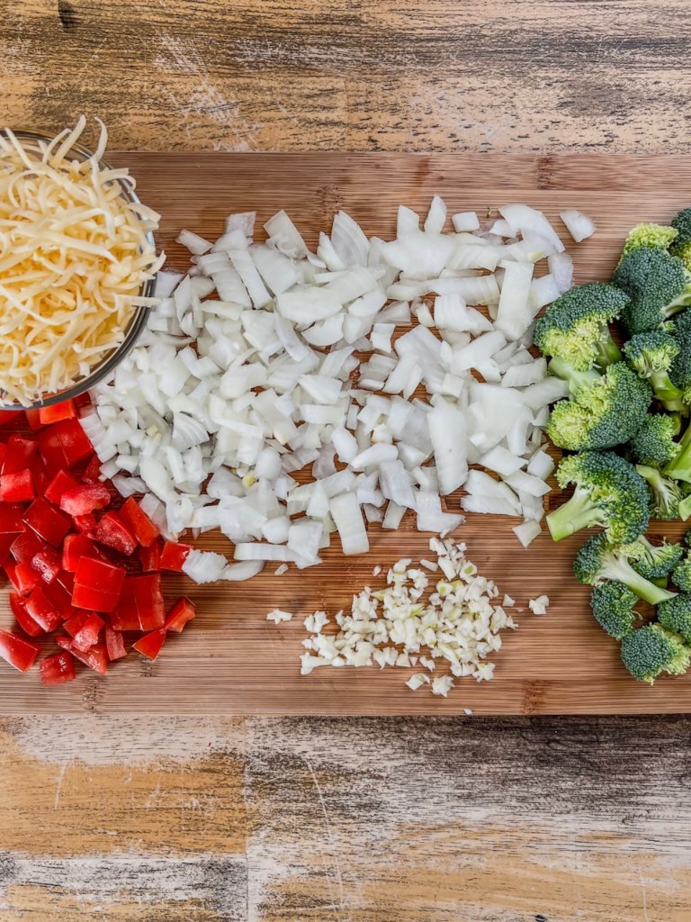 Broccoli, onion, garlic, tomato, and cheese prepped on a cutting board