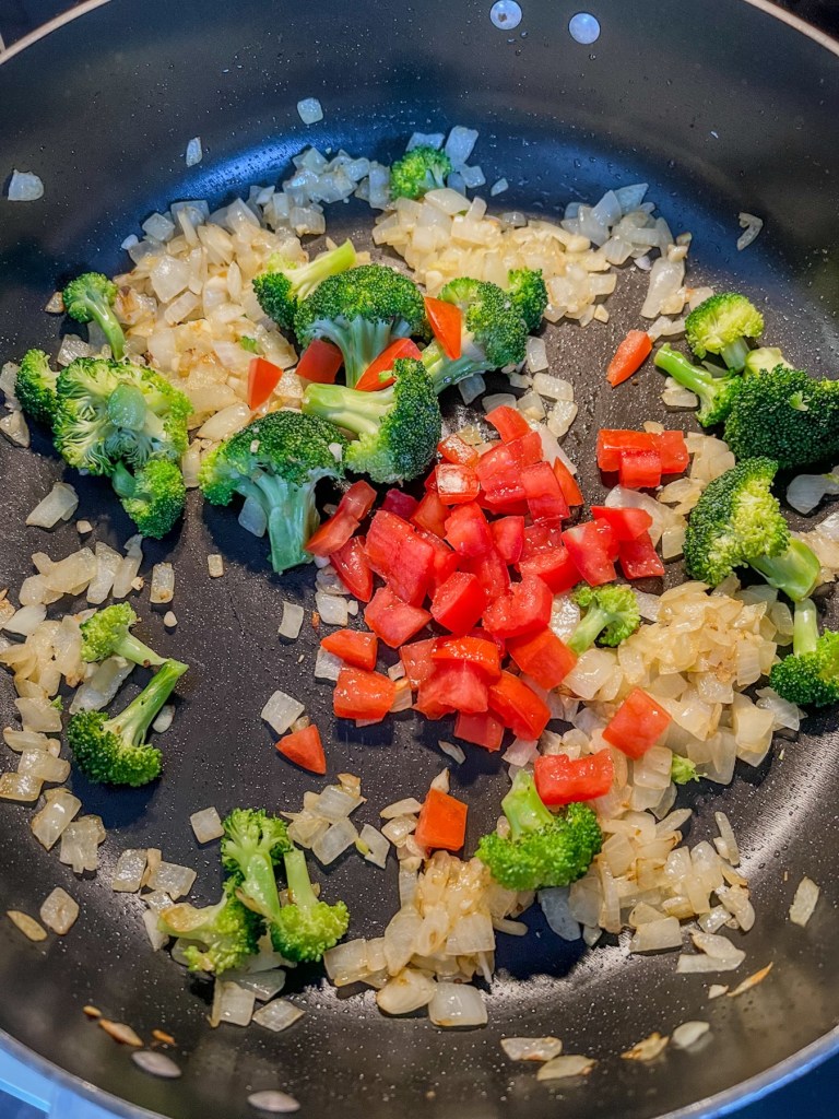 Onion, garlic, tomato, and broccoli cooking in a skillet on the stove