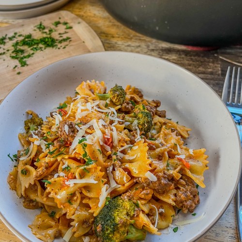 Creamy tomato beef pasta in a bowl with some fresh parsley and parmesan on top with more pasta in a skillet behind
