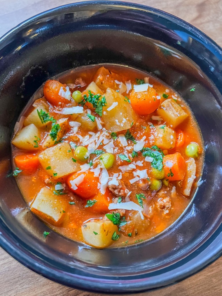 Crockpot Hamburger Stew in a black bowl with fresh parsley and parmesan on top