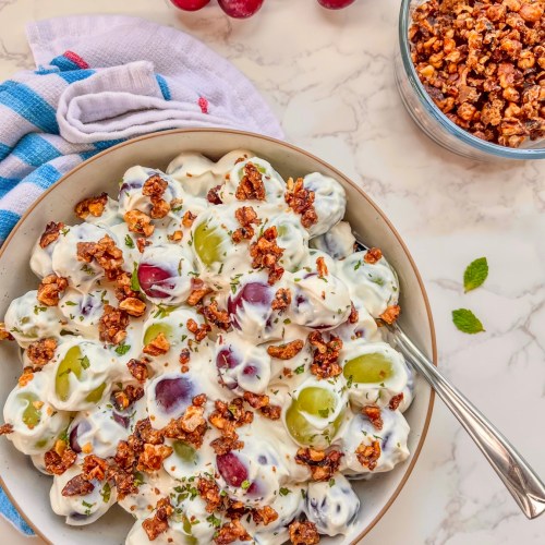 Grape salad with candied walnuts in a bowl with some fresh mint on top and more fixings scattered around