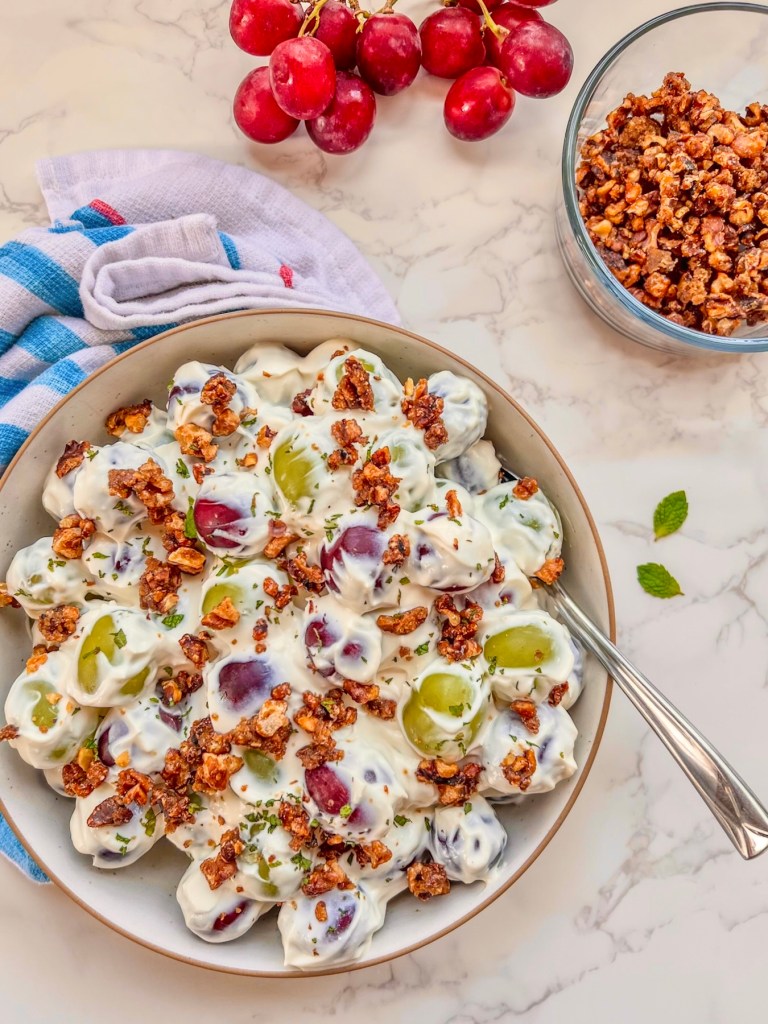 Grape salad with candied walnuts in a bowl with some fresh mint on top and more fixings scattered around