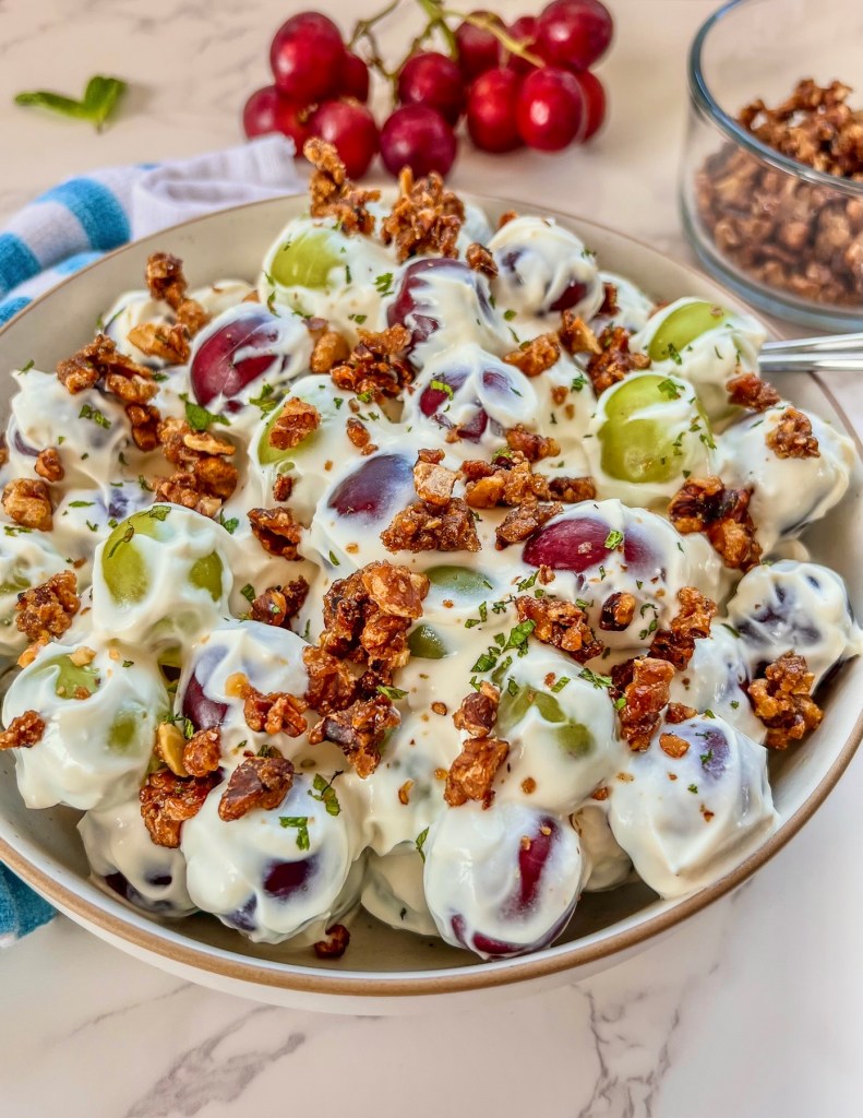 Grape salad with candied walnuts in a bowl with some more grapes and walnuts off to the side