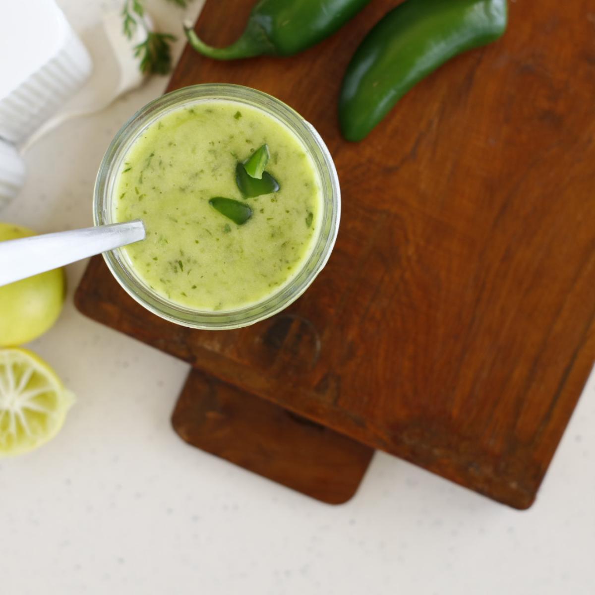 Jalapeño vinaigrette in a dish with some fresh herbs on top and some peppers off to the side