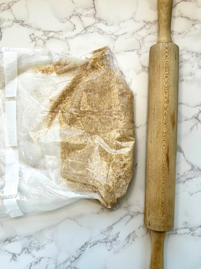 Crushed graham crackers in a Ziplock bag with a rolling pin next to it