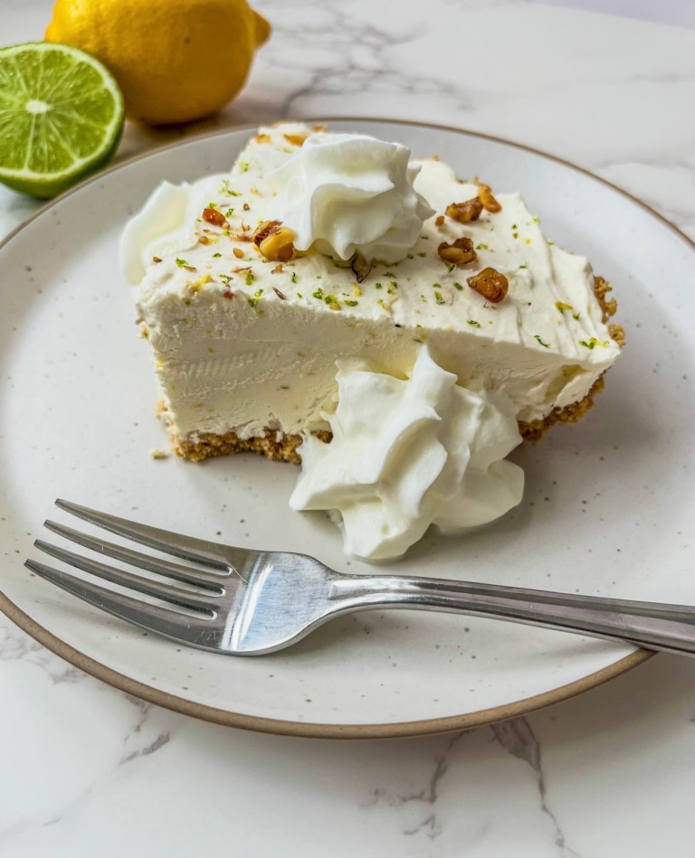 Lemon lime no bake cheesecake sliced with some whipped cream, lemon and lime zest, and toasted walnuts on top