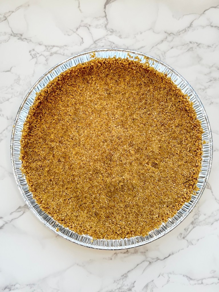 Homemade graham cracker crust in a pie pan before going into the refrigerator to chill