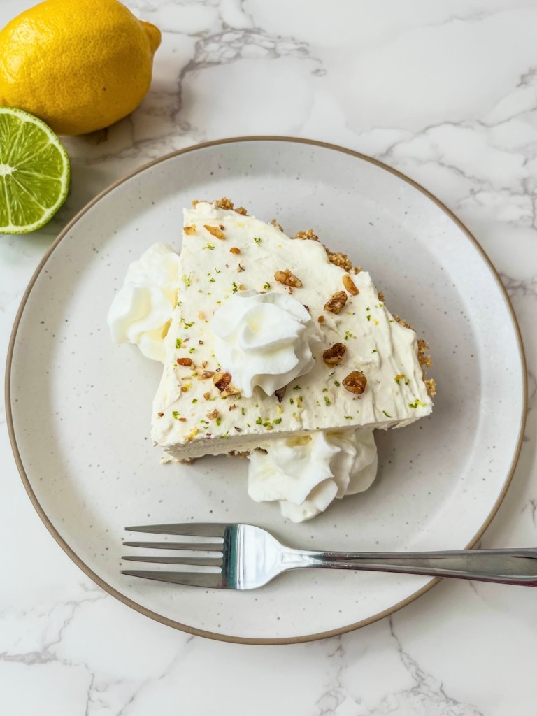 No bake cheesecake with whipped cream and toasted walnuts on top with some lemon and lime off to the side