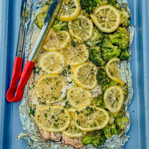 Salmon and broccoli foil pack opened up on a blue baking sheet after just being grilled