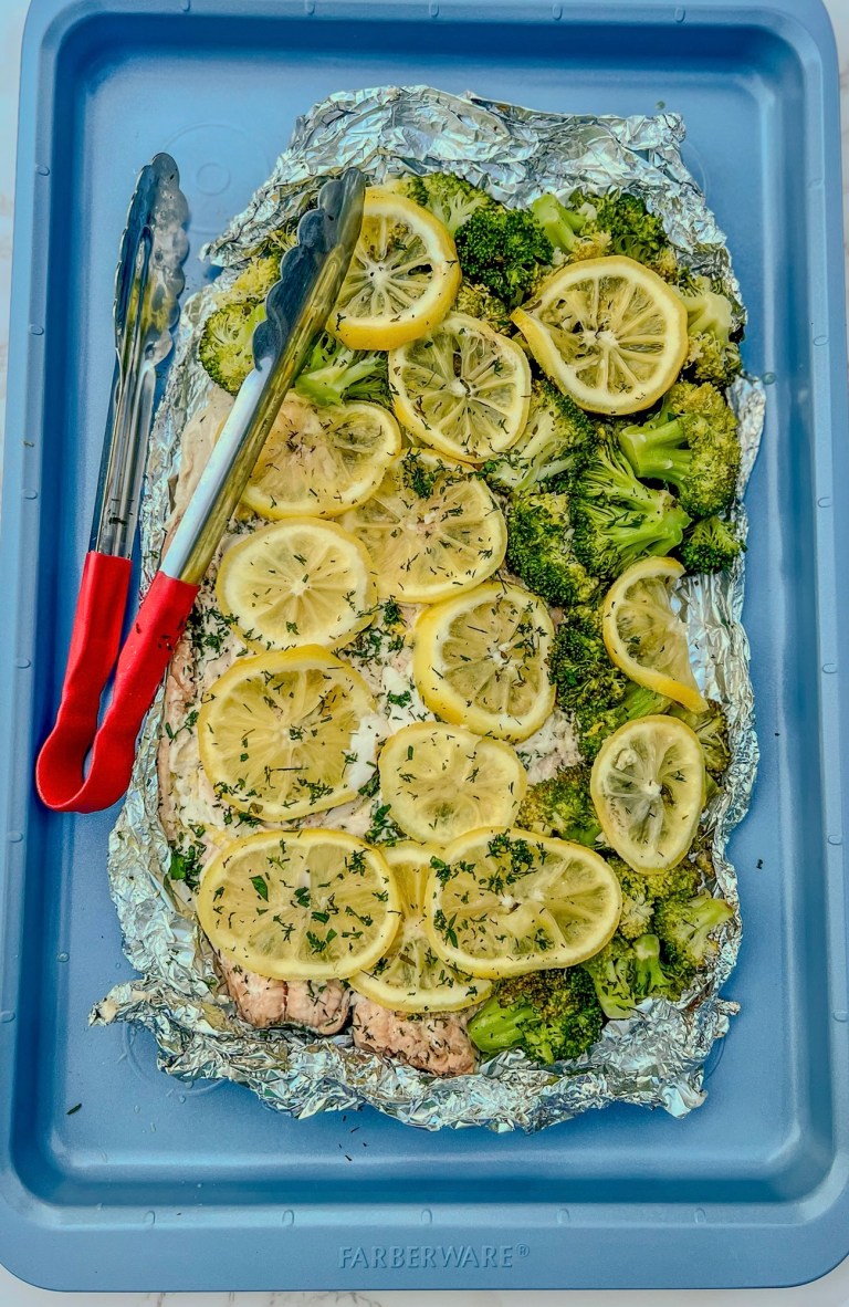 Salmon and broccoli foil pack opened up on a blue baking sheet after just being grilled