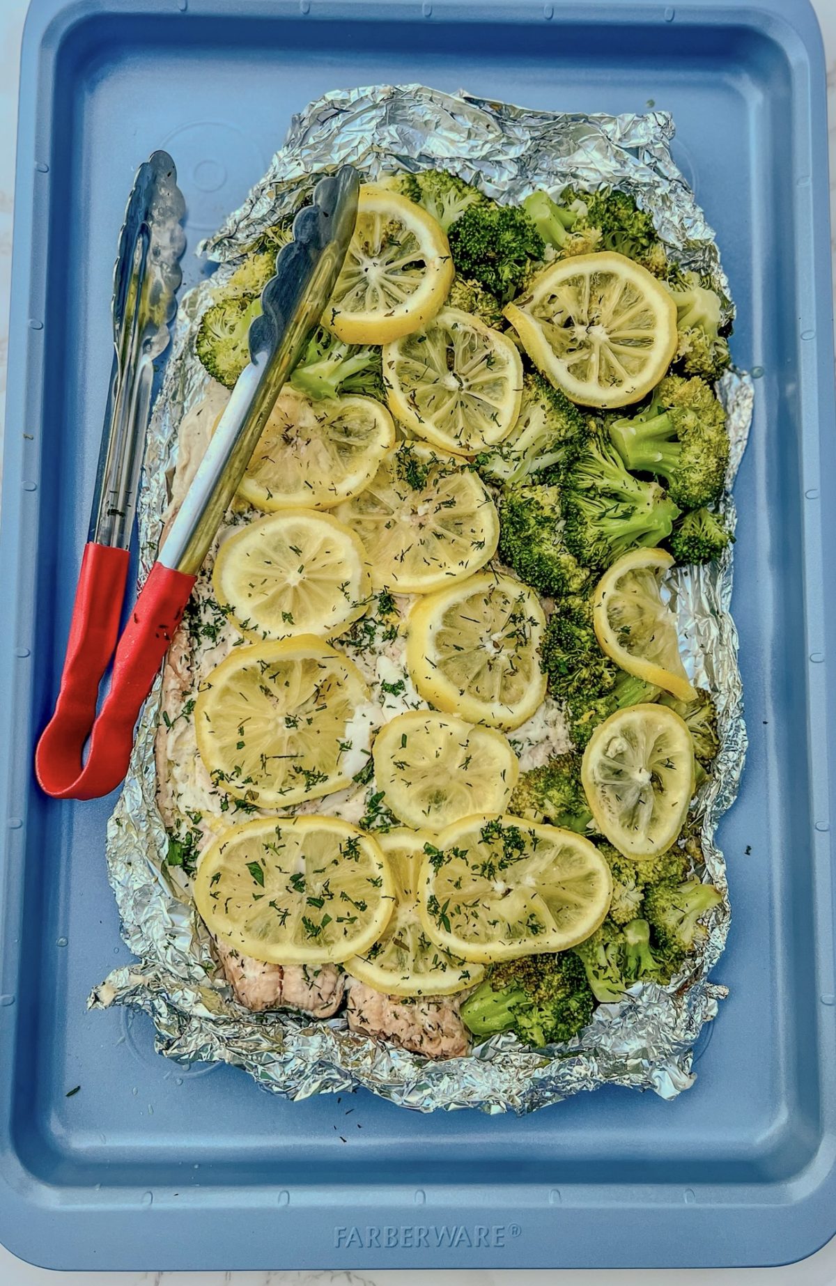 Salmon and broccoli foil pack opened up on a blue baking sheet after just being grilled